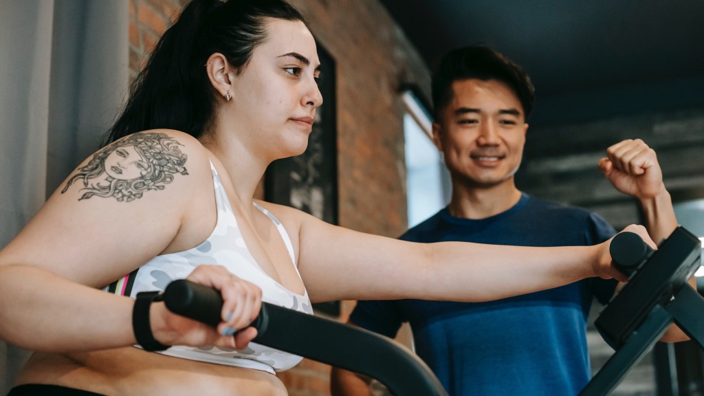 Female on bike getting over her beginners gym anxiety, alongside a coach